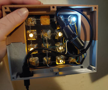 The back of the clock again, with more parts added: deeper walls, a circuit board wrapped in electrical tape, wires, and a cable mounted to the bottom.