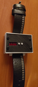 A silver plastic box with a black plastic face and a leather strap. There are a small red indicator and two silver buttons in the face of the box.