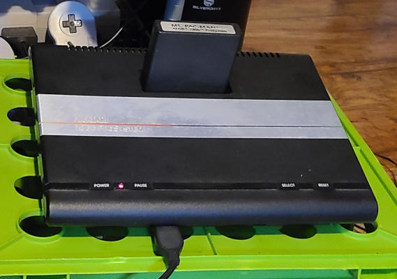 A sleek black wedge with a silver band across it. There is a thin rainbow stripe across the silver band. There is a row of buttons along the front top, and a cartridge protrudes from the rear top. Something is plugged into the front.