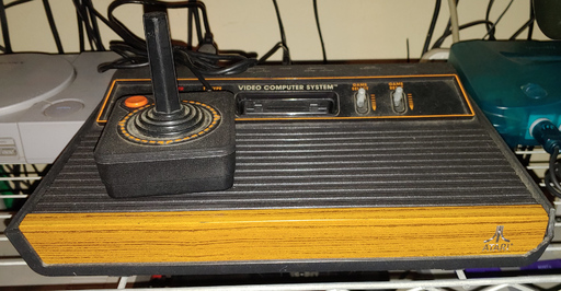 An angular, ridged, black, plastic box with a wood accent. A black plastic joystick rests on top.