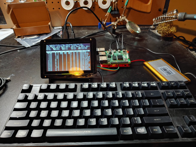 A keyboard, a small computer screen, an exposed circuit board and a battery, connected by cables.