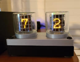 Two glass tubes stick out of the top of a thin silver and black box. The numbers '7' and '2' glow orange from behind metal grids inside the tubes.