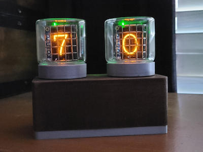 Two glass tubes sit on a wood box. The numbers '7' and '0' glow orange from behind metal grids inside the tubes.