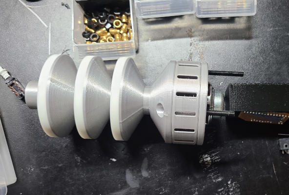 The silver barrel of the raygun. It is attached here only to a flared base and a cylindrical piece with oblong holes in it. The back of a speaker and some bolts stick out of the other end of the cylindrical section.