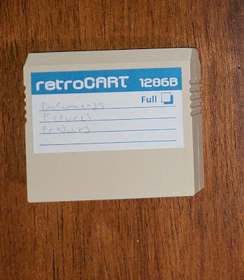 A biege plastic cartridge with a paper label listing the files it contains.