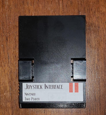 A black plastic cartridge labeled 'Joystick Interface: Nintendo.' Each side has a separate piece of plastic mounted in a cutout.