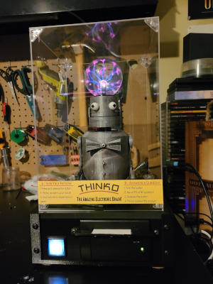 A silver robot with bulbous eyes, a plasma ball for a  cranium, and a metal bow-tie. Underneath it is a black box with a button and small receipt printer.
