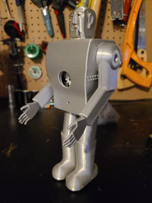 A silver robot with a head sculpted in a stylized human-like shape. Gears are visible through a hole in its boxy torso.
