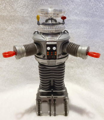 A robot with a translucent disk head, a cylindrical silver torso, bellows-like arms and legs, and large trapezoidal silver feet