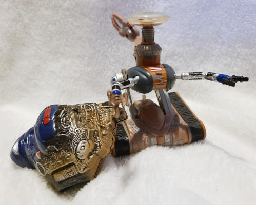 A robot with a translucent disk head, a small streamlined torso suspended above tank treads, and three claw arms. A damaged streamlined blue torso with a single red eye sits next to it.