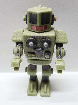 A pale green robot with armas and legs. It's eyes are rectangular mesh, and it has a model of a reel-to-reel tape unit on its chest.'