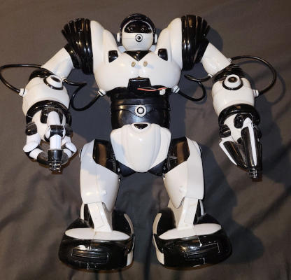 A robot with short legs, big arms and feet, and a small head. There are some metal posts and wires coming out of its chest.