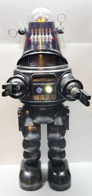 A figure with stubby arms, bulbous legs, and a glass-domed head. A panel in its chest has lights and switches.