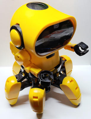 A yellow and black plastic robot with a large rounded head, two arms, and six legs.