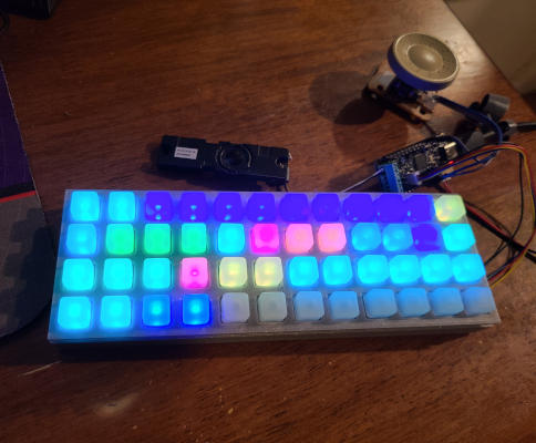 A speaker, a circuit board, an encoder knob, and 12x4 grid of light-up square buttons, all connected by thin wires.