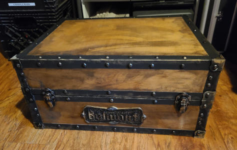 A weathered wooden box with black 'metal' straps and rivets. A plaaque on the front reads 'Belmont'.