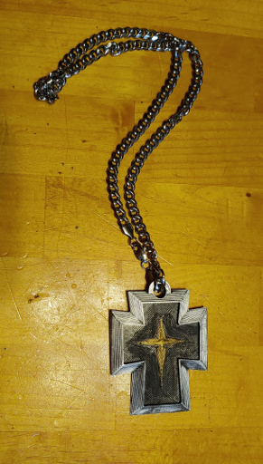 A black cross with silver edges and a gold star-burst in the middle. It is on a heavy silver chain.