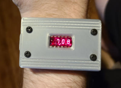 A rectangular watch with a silver face. A tiny red seven-segment-display in the center displays '7.08.'.